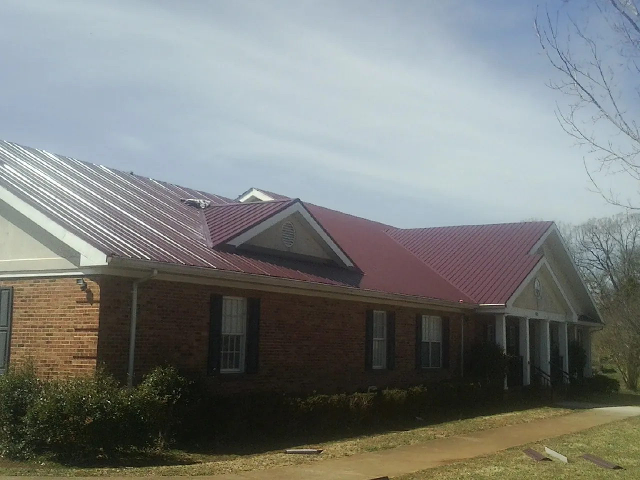 Red metal roof with gabled entries on a long brick building, from a Hail Damage Roof Repair job in Taylorstown