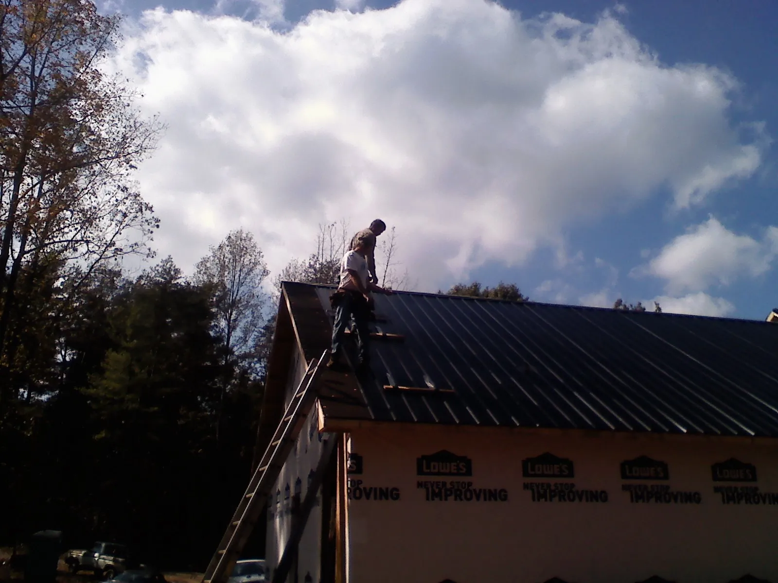 Roofer fastening dark metal panels high against a cloudy sky, from a Roof Inspection job in Taylorstown