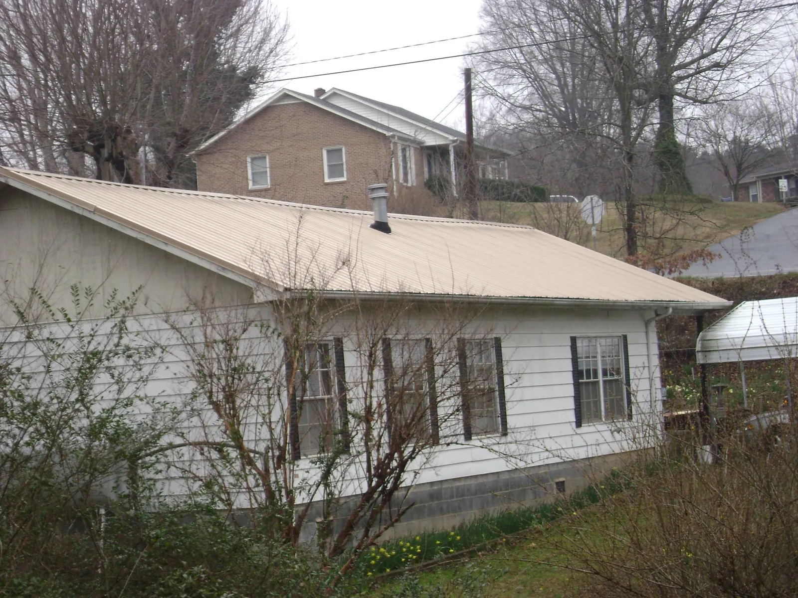 Tan metal roof on a white sided house set into a hillside — Commercial Roofing by Roofing Brothers in Taylorstown